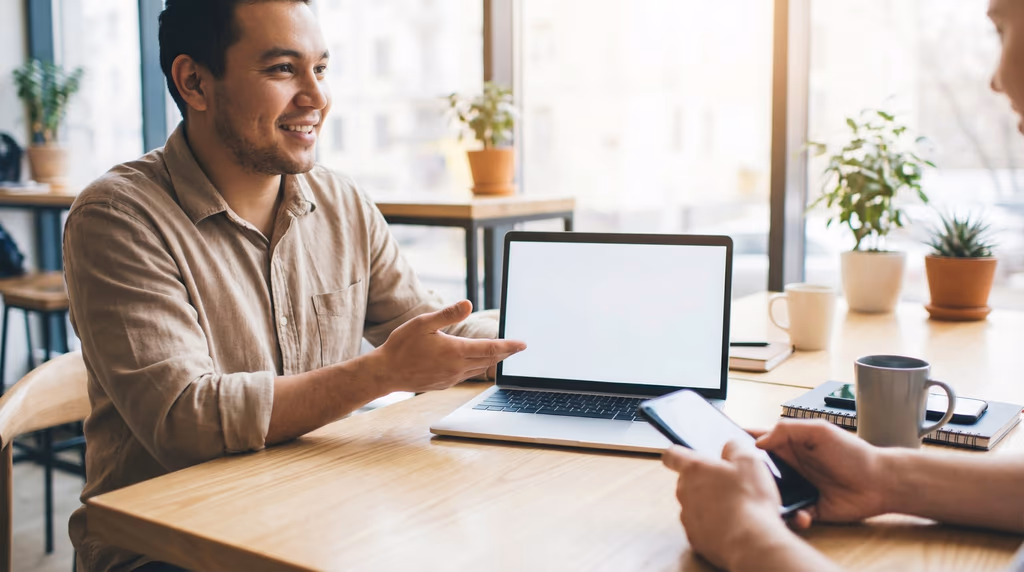 Two individuals are engaged in a conversation at a table with digital devices.
